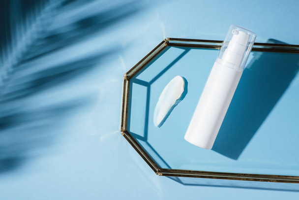 Losyon için pompalı plastik beyaz tüp ve kremin mavi arka plandaki cam tepside görünümü. Cilt bakımı ya da güneş kremi kozmetik ürünleri. Yüz bakımı için güzellik konsepti - Fotoğraf, Görsel