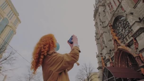 Viajar y covid. Mujer pelirroja en máscara protectora hace selfie contra el telón de fondo de las vistas. - Metraje, vídeo