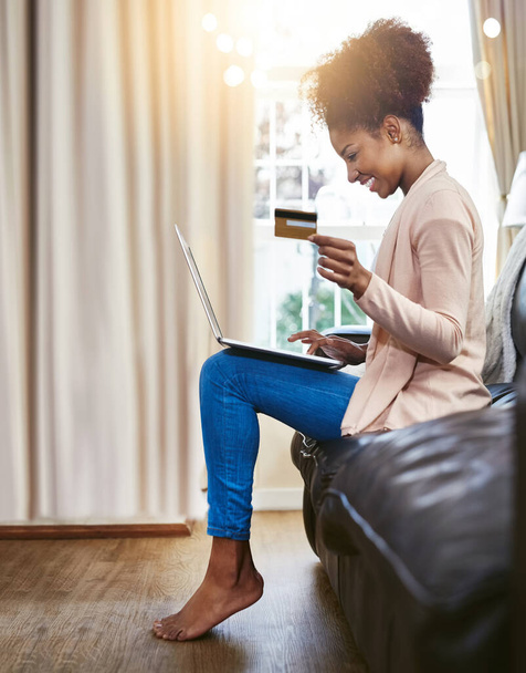 Time to spend some money. Shot of an attractive young woman shopping online while chilling at home on the sofa. - Photo, image