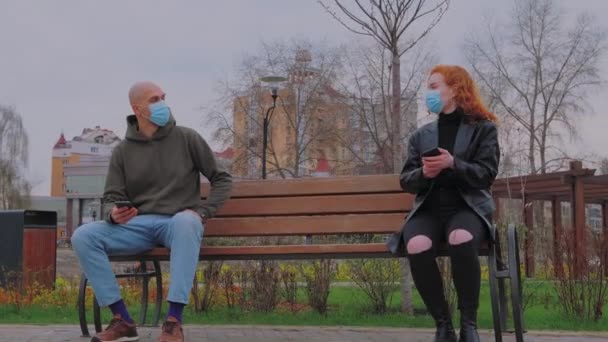 Hombre y mujer sentados en el banco del parque se quitan sus máscaras protectoras y comienzan a comunicarse.  - Metraje, vídeo