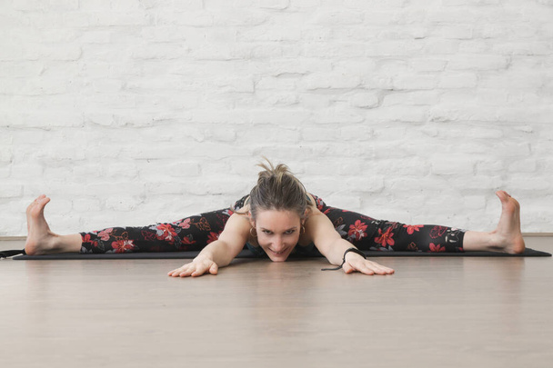Yoga pozisyonlarını esneten genç bir kadın. Önde derin bir yarık. Refah ve kendine bakım kavramı. - Fotoğraf, Görsel