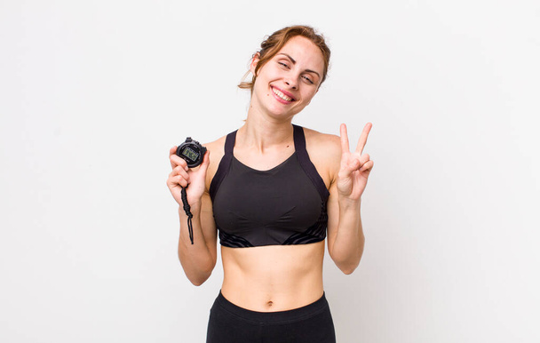 young pretty woman  smiling and looking friendly, showing number two. fitness concept and stopwatch - Photo, Image