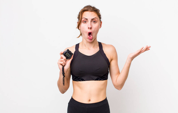 young pretty woman  looking surprised and shocked, with jaw dropped holding an object. fitness concept and stopwatch - Foto, Imagem