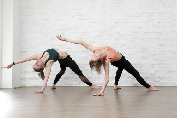 Two young women practicing stretching yoga positions in yoga studio. Wellbeing and self care concept. - Fotó, kép
