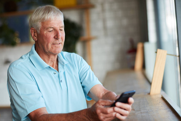 A kávézóban várok rád. Vágott kép egy idős emberről, aki a mobilját használja, miközben egy kávézóban ül.. - Fotó, kép