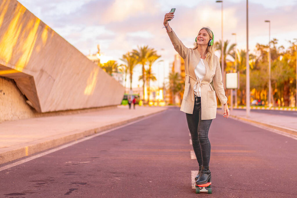 Young business woman having fun on a skateboard outdoors, listening music with smartphone and wireless headphone. Job and ecology future concept. - Фото, изображение