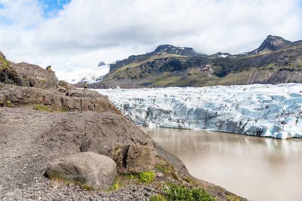Ледовое поле в Исландии в частично облачный летний день. С левой стороны на фотографиях видны туристы, любующиеся ледником. Ватнайокулл, Исландия. - Фото, изображение