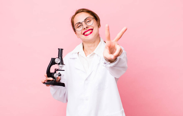 young pretty woman  smiling and looking happy, gesturing victory or peace. scientist with microscope concept - Fotoğraf, Görsel