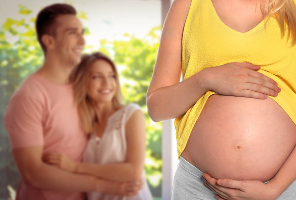 Surrogacy concept. Young pregnant woman and blurred view of happy couple indoors - Foto, Bild