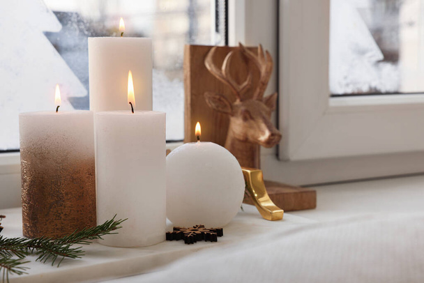 Beautiful burning candles with Christmas decor on windowsill indoors, space for text - Foto, Bild