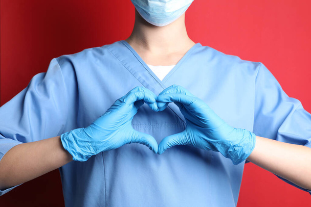 Doctor making heart with hands on red background, closeup - Foto, Bild