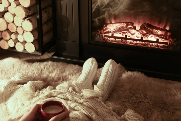 Woman with hot drink resting near fireplace at home, closeup - Foto, afbeelding