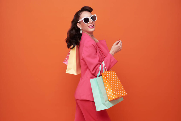 Χαρούμενη χαρούμενη γυναίκα που απολαμβάνει τα ψώνια, κουβαλάει τσάντες με πορτοκαλί φόντο. - Φωτογραφία, εικόνα