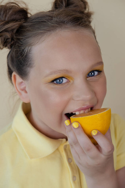 sweet cute girl school age holding a ripe fresh lemon on yellow background. child with fruit on colorful background. summer citrus food - Foto, afbeelding