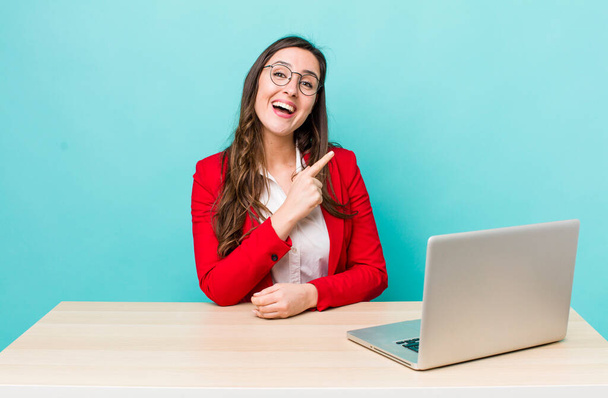young pretty woman  smiling cheerfully, feeling happy and pointing to the side. business desk concept - 写真・画像