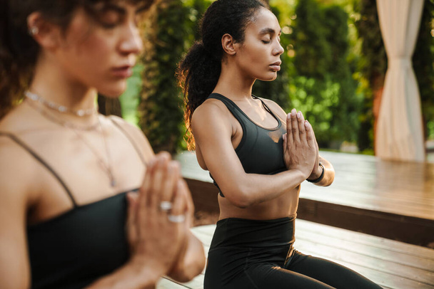 Multiracial two women meditating during yoga practice outdoors - 写真・画像