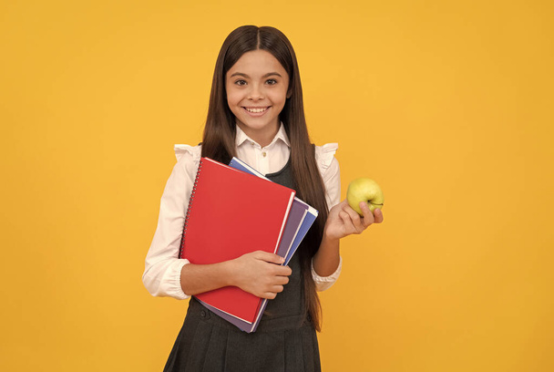 Ευτυχισμένο παιδί πίσω στο σχολείο κρατώντας μήλο και βιβλία κίτρινο φόντο, εκπαίδευση - Φωτογραφία, εικόνα