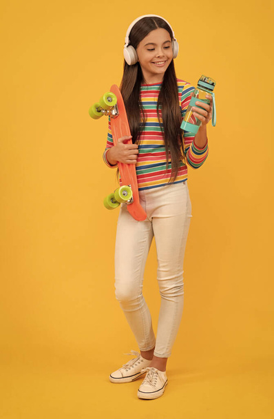 gelukkig tiener meisje skateboarder luisteren muziek in hoofdtelefoon met penny board en water, skater. - Foto, afbeelding