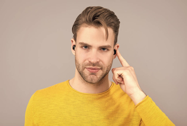 Schöner Kerl zeigt mit dem Finger auf Ohrhörer im ohrengrauen Hintergrund und hört zu - Foto, Bild