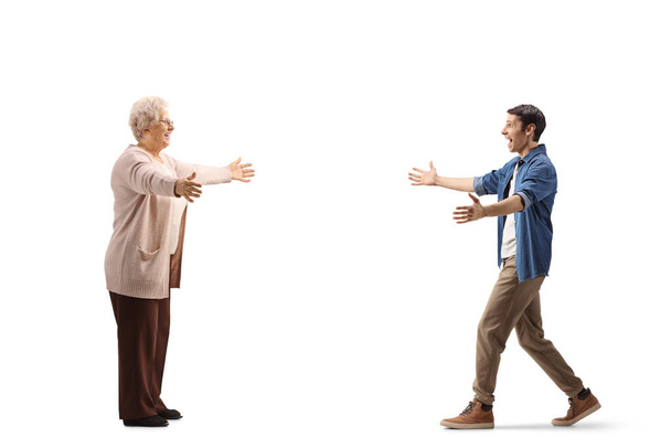 Full length profile shot of a young man walking towards an elderly woman with arms wide open isolated on white background - Foto, Imagem