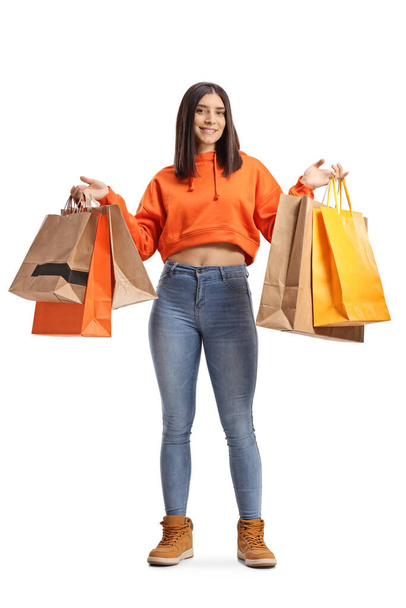 Full length portrait of a young female in jeans and orange sweathshirt holding shopping bags isolated on white background - Foto, Bild