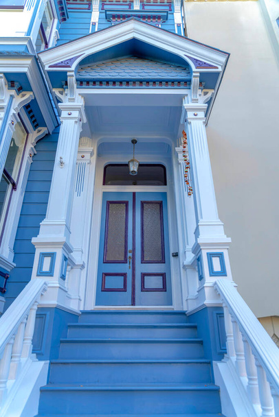 Вход в таунхаус в Сан-Франциско, штат Калифорния, украшен наличниками в восточном стиле. Есть лестница с синими ступеньками, ведущими к двойной двери с транцевым окном под подвесным потолком. - Фото, изображение