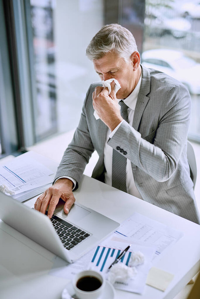 Het is niet productief om ziek te zijn op het werk. Gehakt schot van een zieke zakenman snuit zijn neus in het kantoor tijdens het werken aan een laptop. - Foto, afbeelding