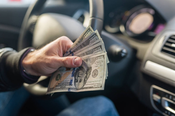 manos fuertes masculinos sosteniendo billetes de dólar en el centro en el interior del coche en el fondo del volante. Concepto de negocio. El concepto de comprar un coche - Foto, imagen