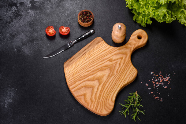 Uma placa de corte de madeira com uma faca de cozinha com especiarias e ervas em um fundo de concreto escuro. Cozinhar em casa - Foto, Imagem