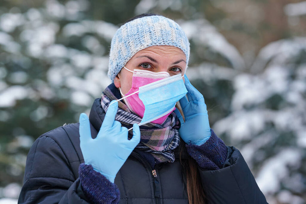 Young woman in warm winter clothing wearing pink disposable virus face mask, putting another one on - some advise that two layers provides better protection again coronavirus covid-19 spread - Fotografie, Obrázek