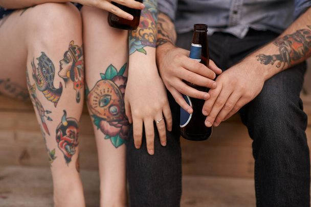 Τα τατουάζ είναι μια άλλη μορφή γλώσσας του σώματος. Ένα ζευγάρι με τατουάζ στο σώμα τους και ποτά στα χέρια.. - Φωτογραφία, εικόνα