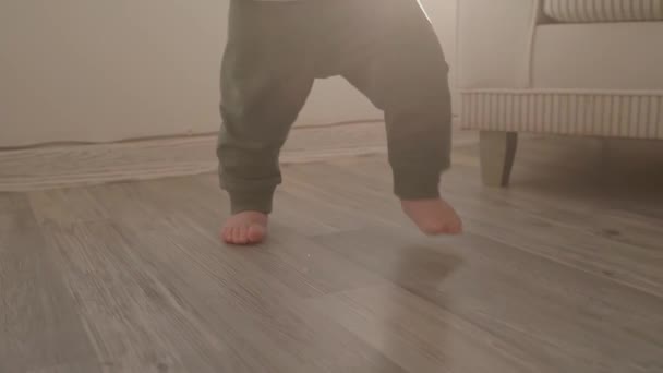 Małe dziecko nagie stopy spacerujące po podłodze, zbliżenie. Dziecko uczy się chodzić, robi pierwsze kroki przed kamerą, robi postępy. Zwolnij trochę. Wnętrze pokoju. Koncepcja dzieciństwa i niemowlęctwa - Materiał filmowy, wideo
