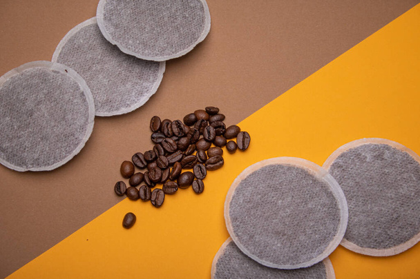 コーヒー生産物の一例として45度の角度でオレンジと茶色の段ボール上のコーヒーパッドとコーヒー豆のトップビュー。平面構成 - 写真・画像