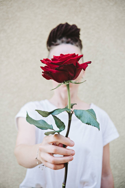 Gezichtsloos portret van een vrouw met een rode roos in de hand. Close-up van vrouwelijke handen die Rose vasthouden. Hipster vrouw hand met een rode roos - Foto, afbeelding