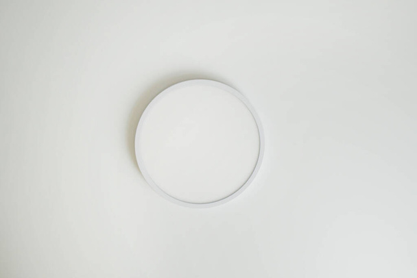 Round, minimalist, simple lamp on a white ceiling. A lamp that does not attract attention - Fotó, kép