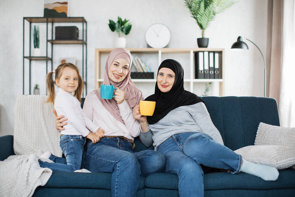 Cute girl, islamic mom and grandma hold mugs of hot drinks. - Valokuva, kuva