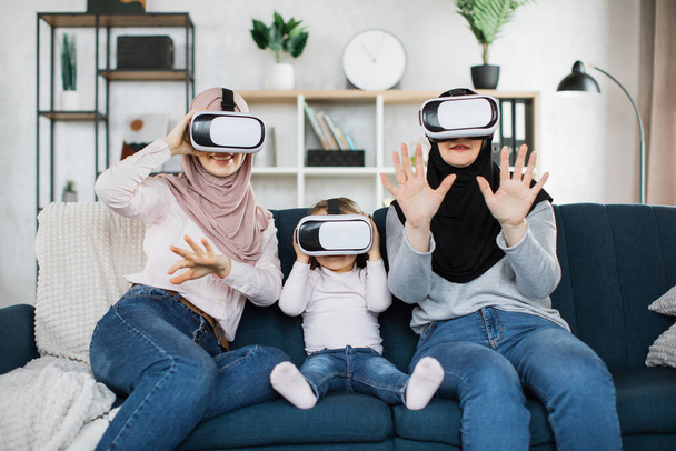 Happy three generations of muslim women watching in modern augmented vr headset reality glasses - Фото, изображение