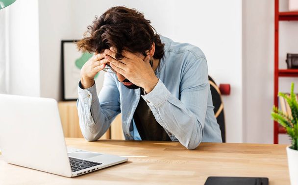 Stressed man with laptop sitting on desk at home office - Fotoğraf, Görsel