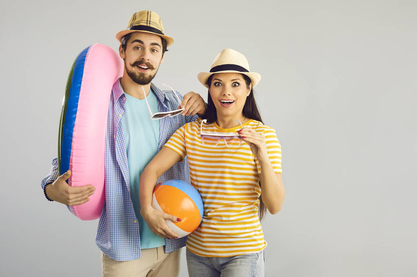 Pleasantly surprised couple standing with an inflatable circle and a ball on a gray background. - Foto, imagen