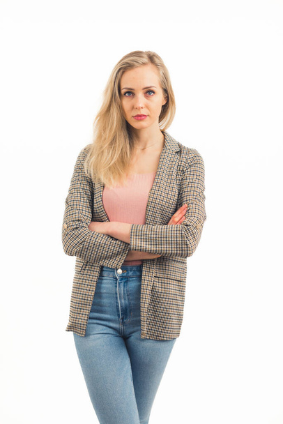 pretty European blonde girl standing with arms crossed and looking critically into the camera wearing sneakers denim jacket and pink shirt studio shot medium full shot white background copy space - Photo, Image