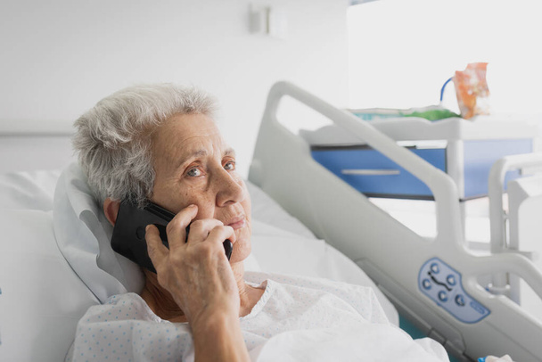 sick hospitalized elderly woman talking on the phone - Foto, afbeelding