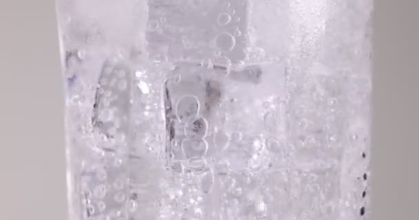 Heldere transparante frisdrank water gieten in een hoog glas gevuld met ijs fizz bel schuim zweven op witte achtergrond  - Video