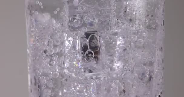 Heldere transparante frisdrank water gieten in een hoog glas gevuld met ijs fizz bel schuim zweven op witte achtergrond  - Video