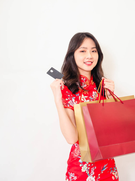 Portrait of a young asian woman wearing traditional cheongsam qipao dress holding shopping bags and showing credit card isolated on wihte background. - Fotografie, Obrázek