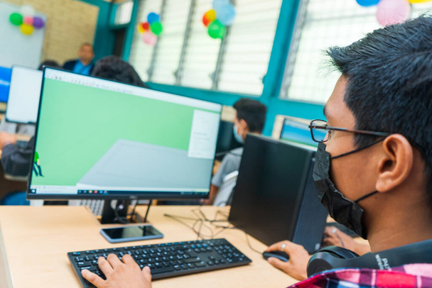 Dark-skinned Central American student in technical education glasses uses a desktop computer to do his homework - 写真・画像
