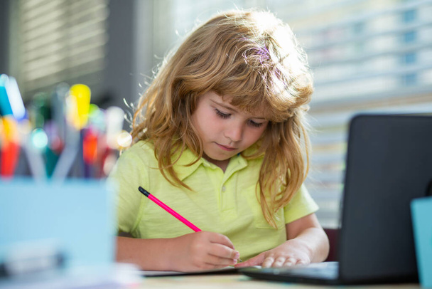 Schooljongen maakt notities in het copybook tijdens online les op laptop thuis. Leuke serieuze jongen die huiswerk maakt. Kinderonderwijs. - Foto, afbeelding