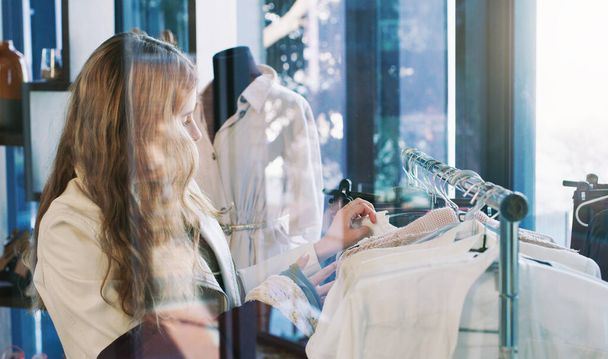 Shop til you drop. Shot of a young woman browsing through clothes in a boutique. - Photo, Image