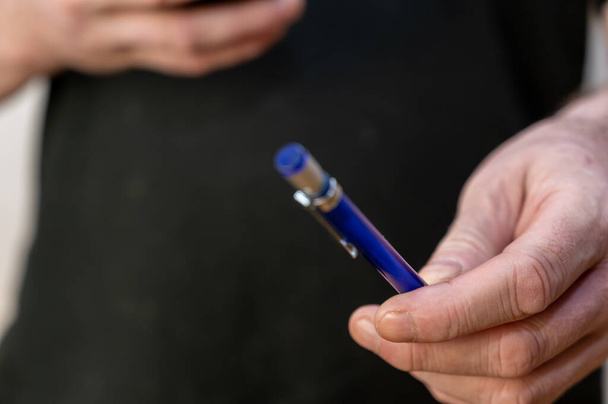 A man's hand holds a blue pen. Middle section of man with ballpoint pen in hand. - Photo, Image