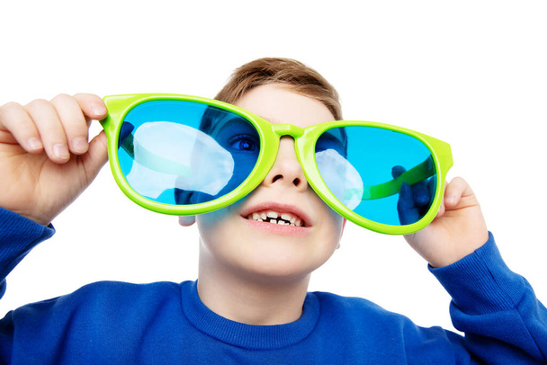 Funny Child in Big Eyeglasses smiling and looking up. Happy Little Boy in Glasses laughing over White Background. Curious Schoolboy in large Spectacles excited - Zdjęcie, obraz