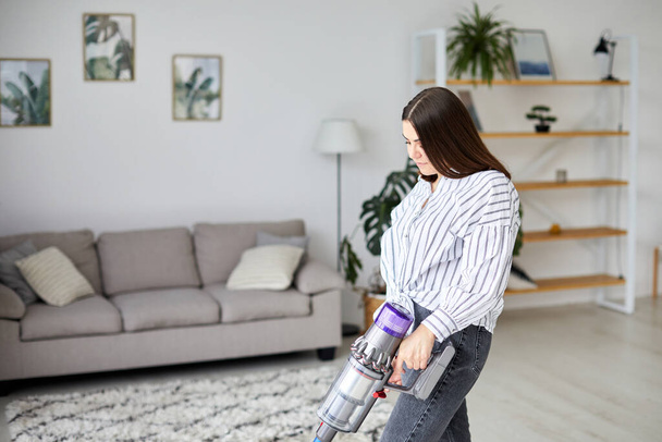 Женщина чистит пол с беспроводным портативным пылесосом в гостиной дома. Домохозяйка делает работу по дому - Фото, изображение